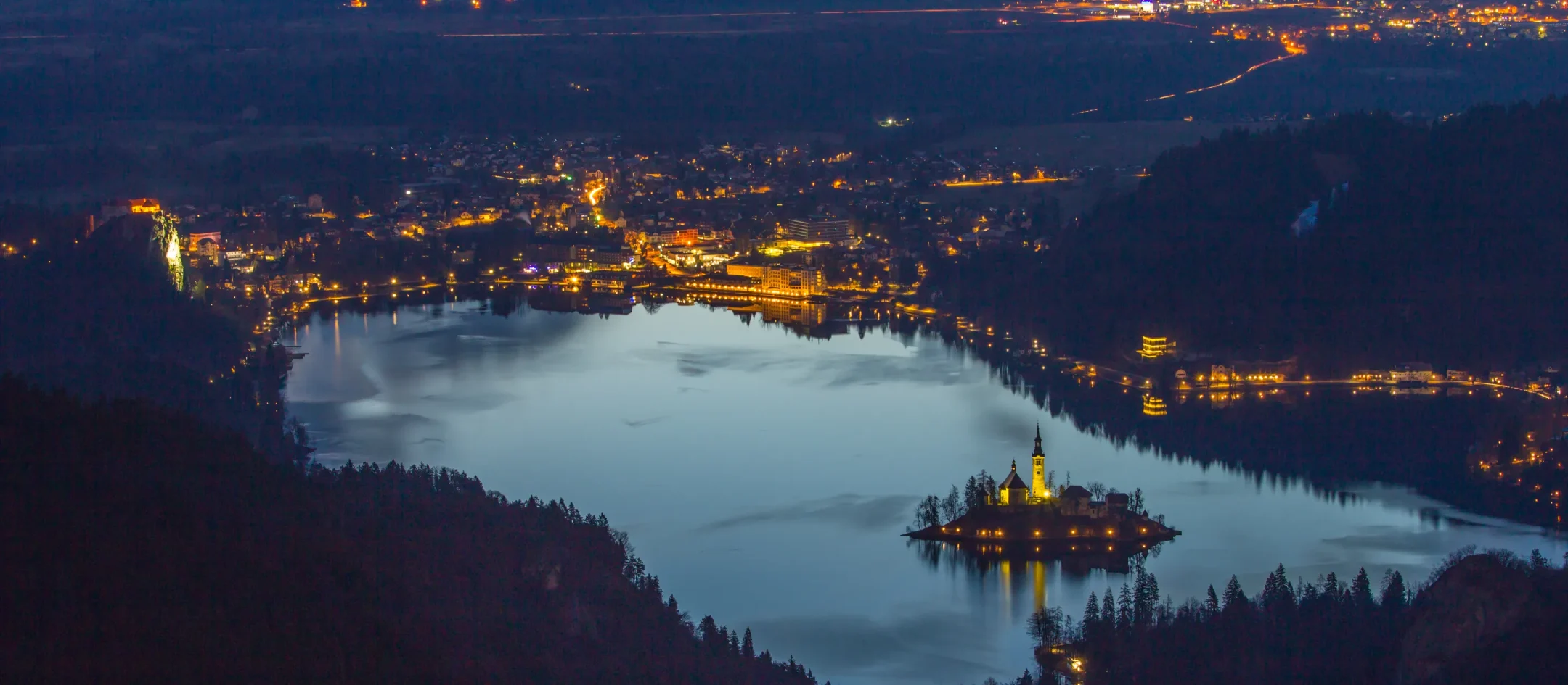 Lake Bled at dusk from above, the lit island on the dark water